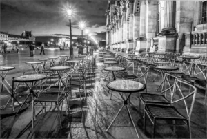 Terrasse de café déserte à Paris, face au Louvre, sous l’éclairage nocturne des réverbères